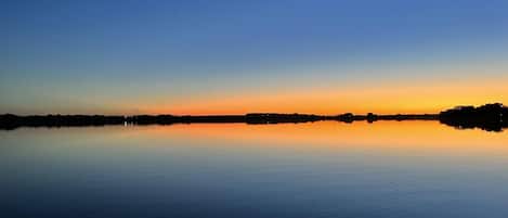 Un lago tranquilo al atardecer con un horizonte despejado y siluetas distantes de la orilla.