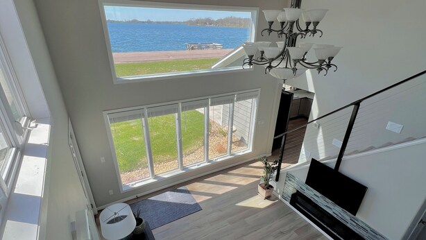 A spacious living room with a large window overlooking a body of water, a built-in fireplace, and a high ceiling with exposed wooden beams.