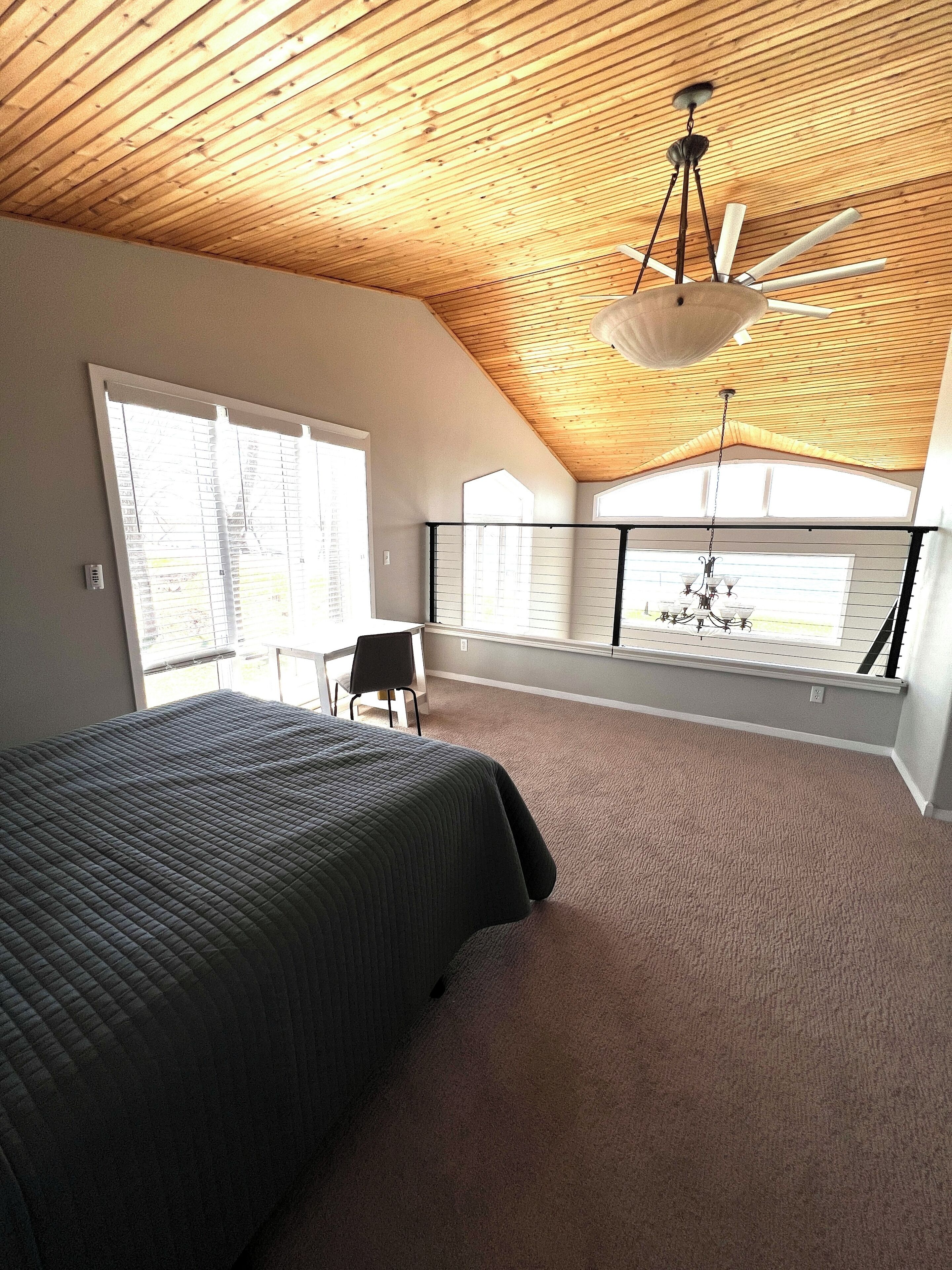 A bedroom with a sloped ceiling, a bed, a chair, and a chandelier.