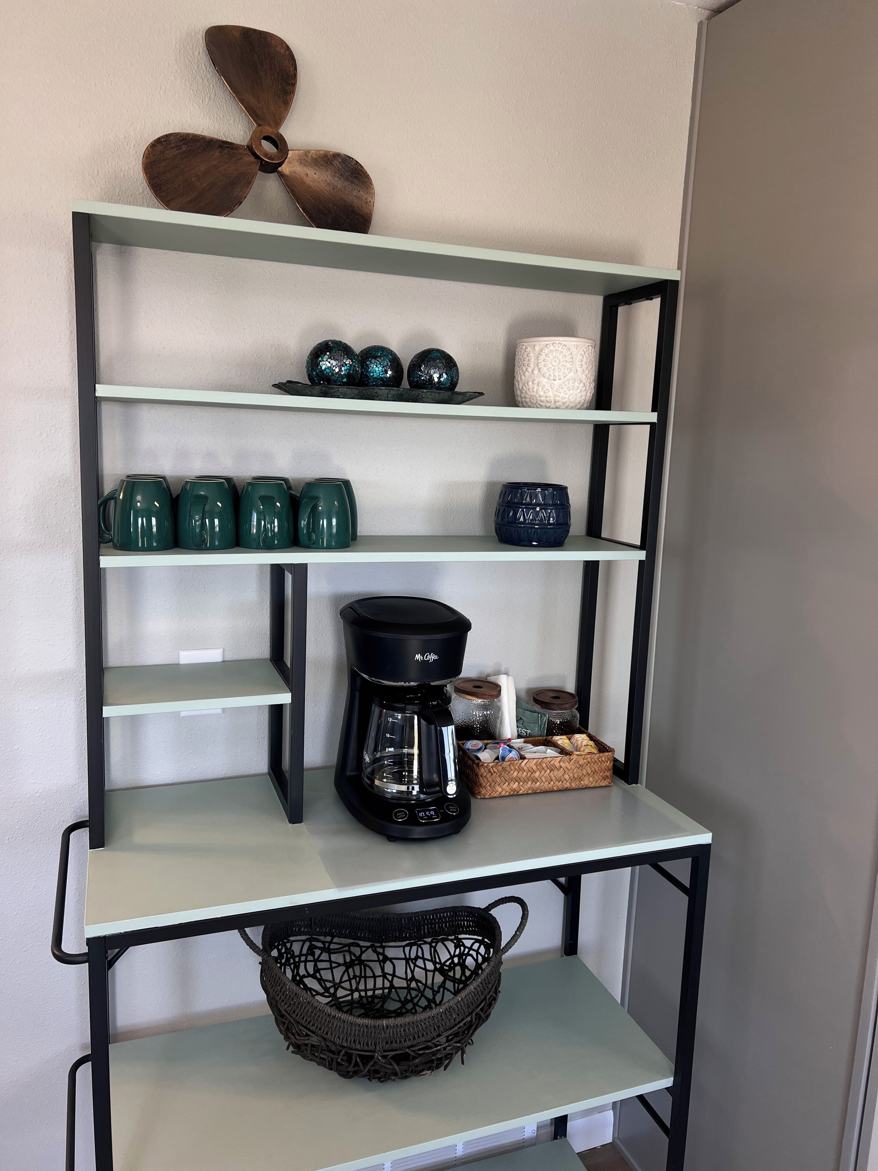 Une étagère de cuisine avec une machine à café, des tasses vertes, des objets de décoration et un panier.