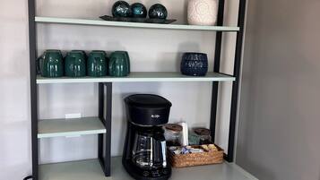 Une étagère de cuisine avec une machine à café, des tasses vertes, des objets de décoration et un panier.