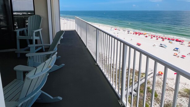 Ein Balkon mit Blick auf den Strand, einer Brüstung und einigen Stühlen.