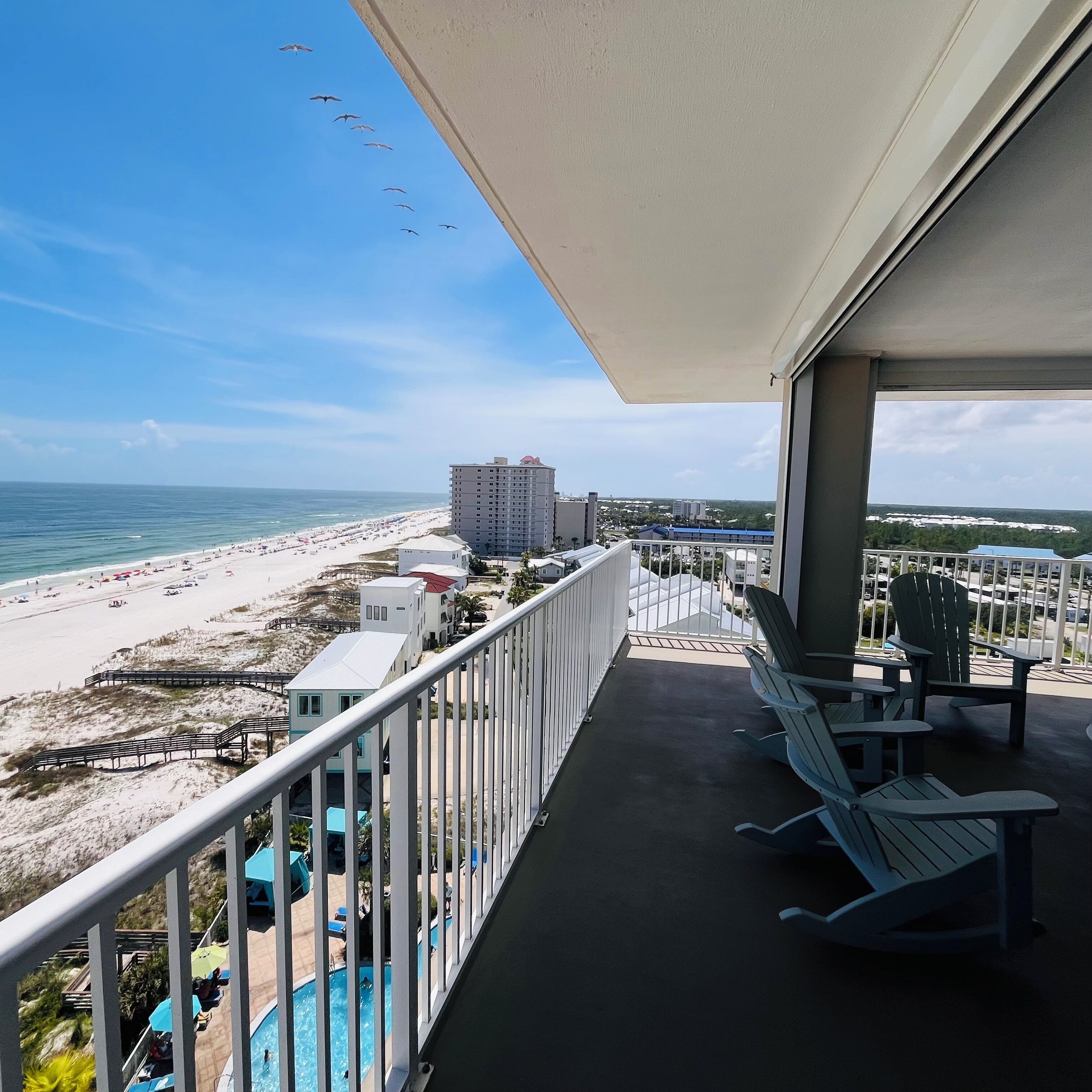 Ein Balkon mit Blick auf einen Strand, ein Schwimmbad und ein Gebäude in der Ferne.