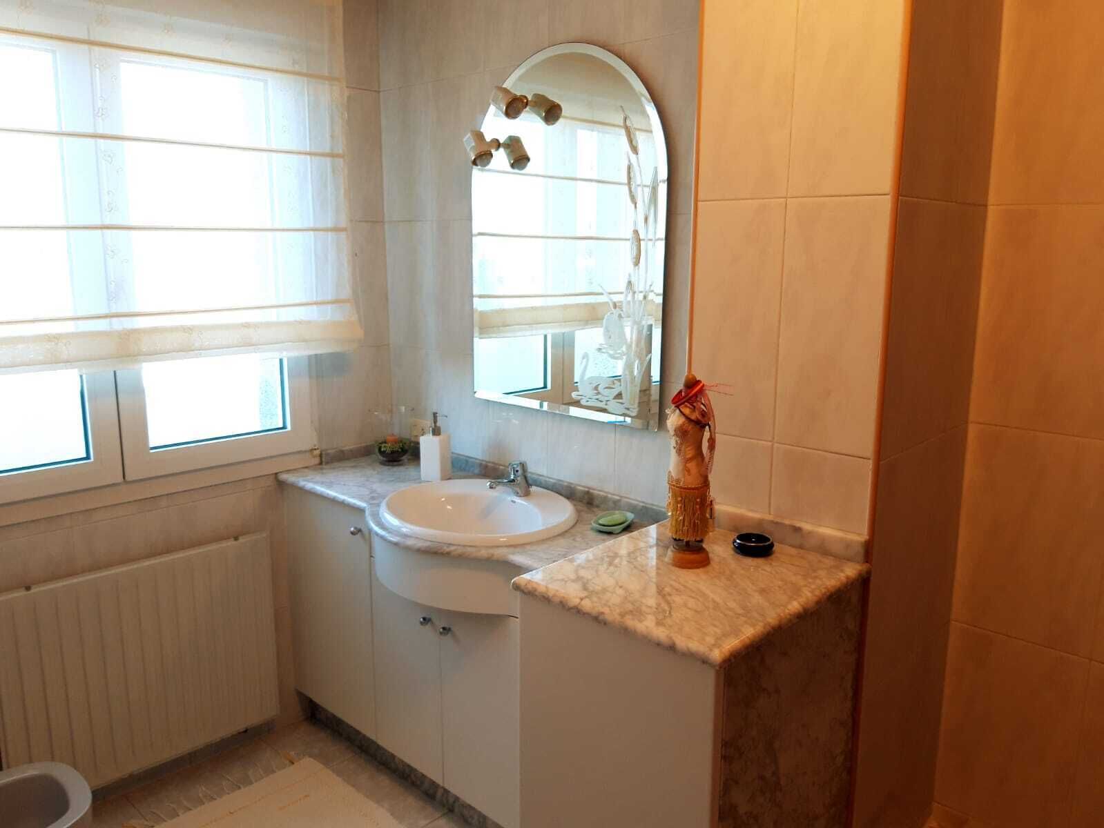 Un baño con ventana, lavamanos, espejo y barra para toallas.