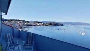 Ein Balkon mit zwei gestreiften Stühlen, Blick auf ein ruhiges Meer mit Booten und eine Stadt im Hintergrund.