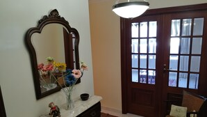 Ein Zimmer mit einem Marmorkonsolentisch, einem Spiegel, einer Blumenvase, einer Holztür mit Glasfeldern und einem Stuhl mit Sitzkissen.