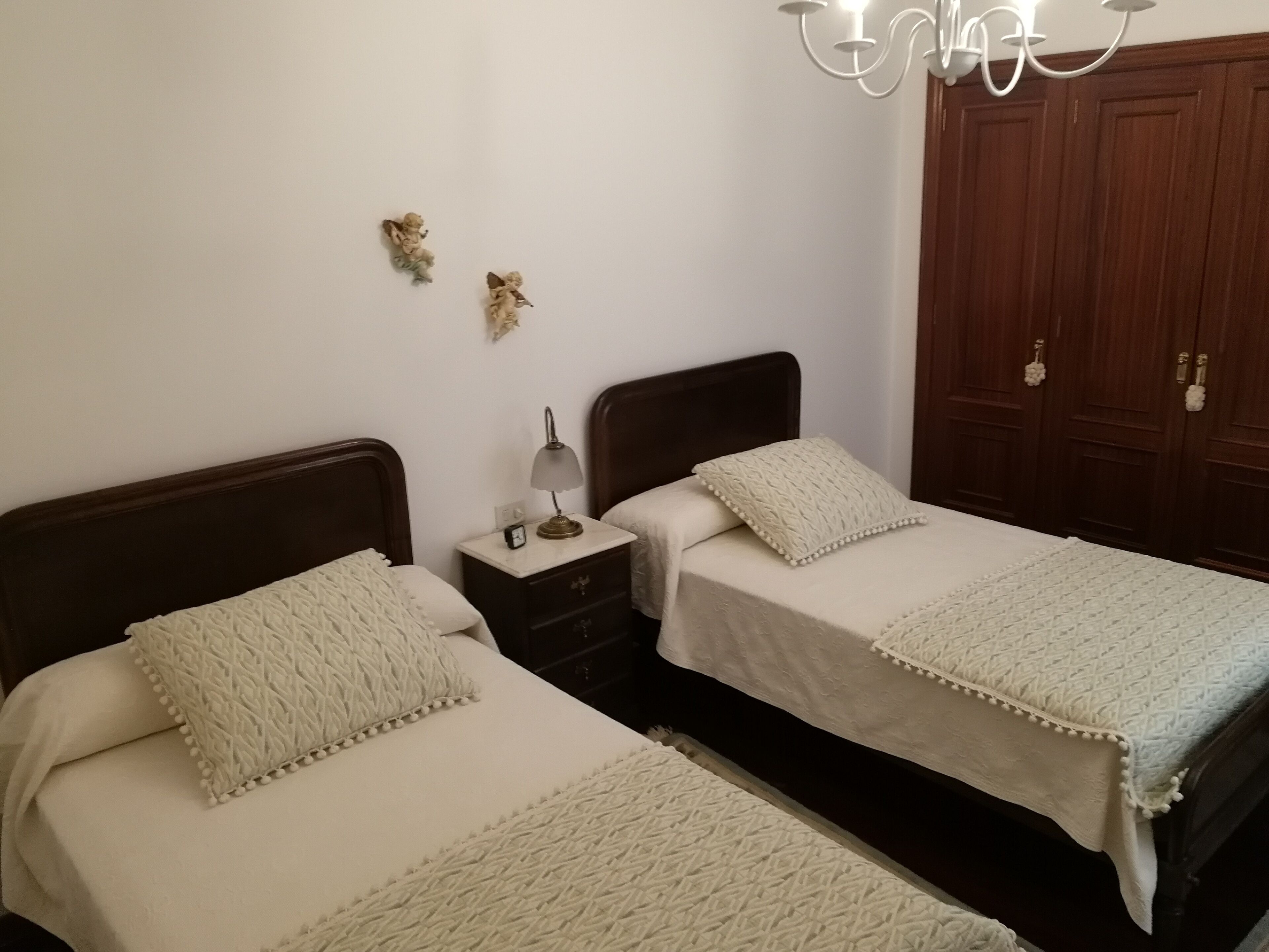 A bedroom with two beds, a nightstand with a lamp, and a wardrobe.