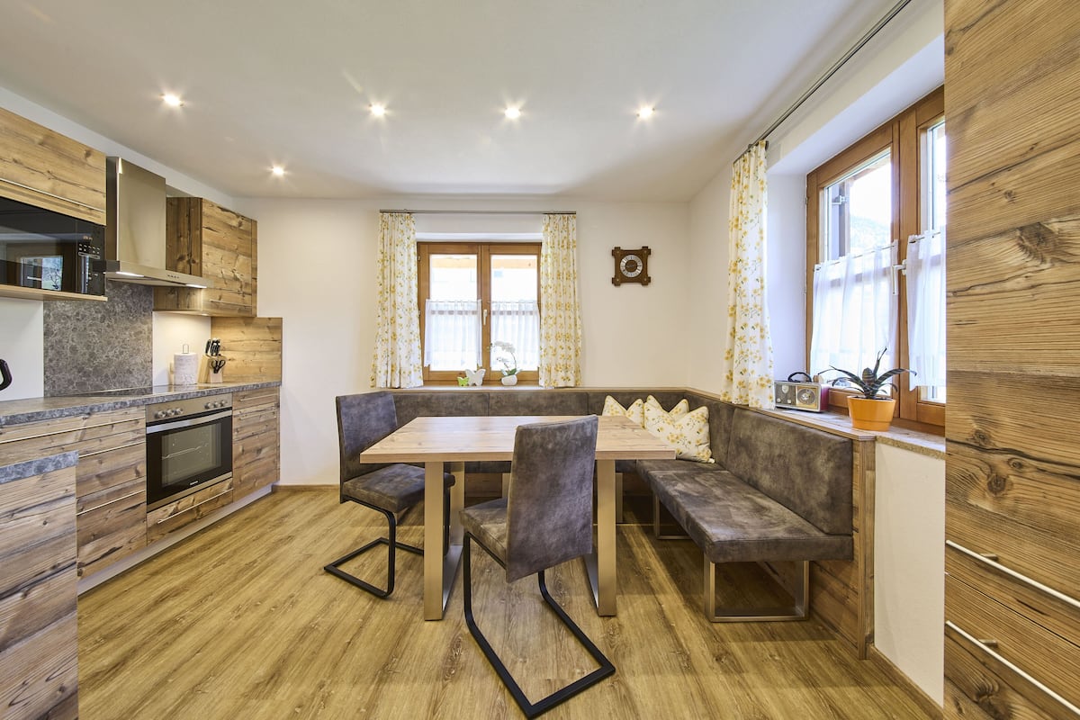 A modern kitchen with wooden cabinetry, a built-in oven, and a dining area with a bench and chairs.