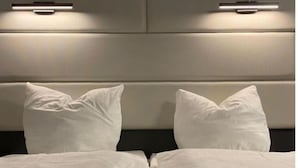 A bed with white linens and pillows, a headboard with integrated lighting, and a neutral-toned wall. - Hotel Continental (Nuremberg)