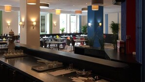A modern restaurant with a long counter, multiple hanging pendant lights, and a mix of indoor and outdoor seating areas. - Hotel Continental (Nuremberg)