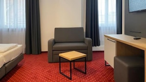 A hotel room with a bed, a desk, a chair, a TV, and a window with curtains. - Hotel Continental (Nuremberg)