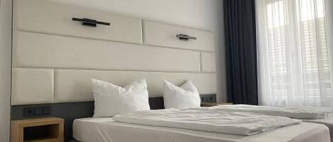 Una habitación de hotel con una cama grande, una mesita de noche y un ventanal con cortinas.