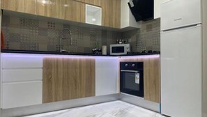 Eine moderne Küche mit Holzausstattung, einer eingebauten Mikrowelle, einem Doppelbackofen und einem weißen Kühlschrank.
