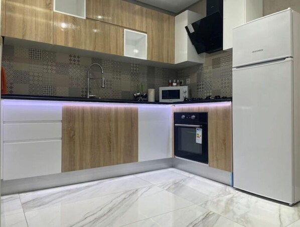 A modern kitchen with wooden cabinets, a built-in microwave, a double oven, and a white refrigerator.