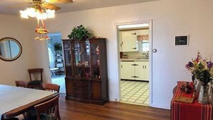 A dining area with a wooden table and chairs, a cabinet with glass doors, and a red tablecloth with a vase of flowers.