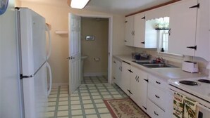 A compact kitchen with white cabinets, a refrigerator, a sink, and a tiled floor.