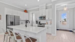 Una cocina moderna con armarios blancos, un refrigerador de acero inoxidable, un microondas y una isla grande con taburetes de bar.