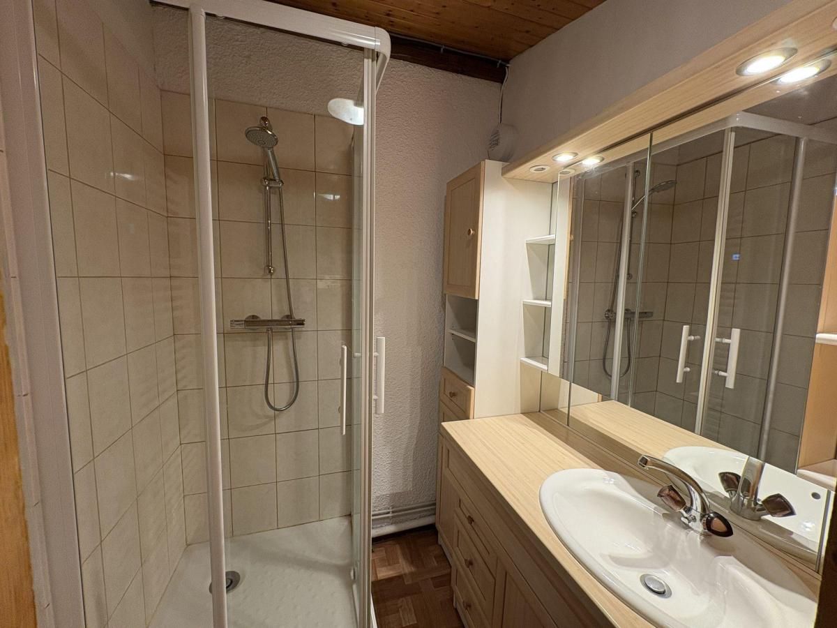 A modern bathroom with a glass-enclosed shower, a large mirror, and a wooden vanity.