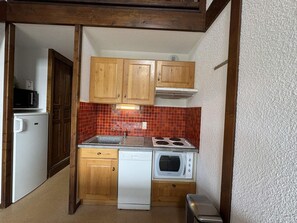 A compact kitchen with wooden cabinets, a white dishwasher, a microwave, and a red-tiled backsplash.