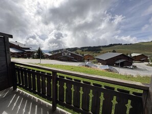 A wooden balcony overlooking a rural landscape with houses and a clear sky.