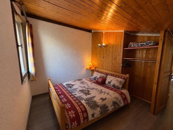 A bedroom with a wooden bed, a wardrobe, and a nightstand with a lamp.