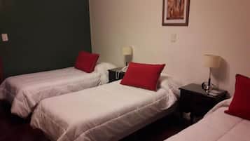 Une chambre avec deux lits simples, chacun agrémenté d’un oreiller rouge et de draps blancs. Il y a des tables de chevet avec des lampes.