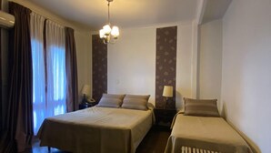 A hotel room with two beds, a bench, a nightstand, a lamp, and a ceiling light fixture.