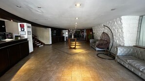 A spacious lobby with a reception desk, a hanging chair, a tufted sofa, and a staircase leading to upper floors.