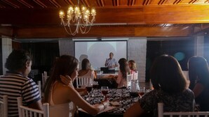 A group of people seated at a table in a restaurant with a speaker at a podium in the background.