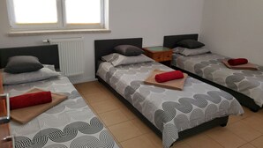 Et værelse med tre senge, hver med mønstret sengetøj og puder, et lille trænatbord og en radiator.