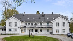 A large, two-story white building with a symmetrical facade, a central entrance, and a small front garden. - Herregårdshuset AS (Ullensaker)