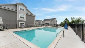 A rectangular swimming pool with a concrete deck, surrounded by a fence and a row of townhouses.