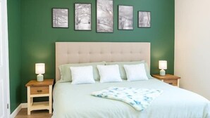 A bedroom with a green wall, a bed with white bedding, and four framed pictures above the bed.