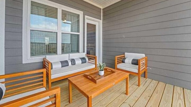 A covered patio with a wooden bench, a wooden table, and a sofa with cushions.