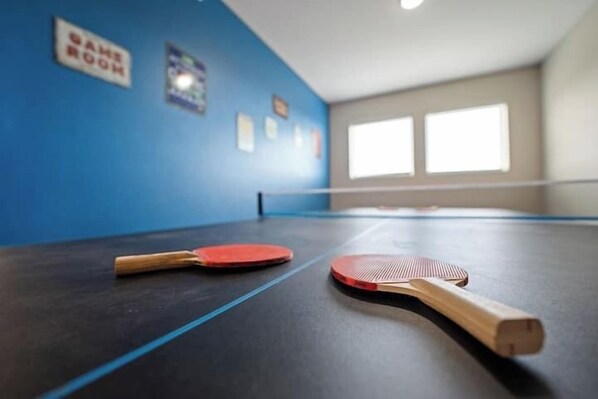 A ping pong table with two paddles and a sign indicating a game room.