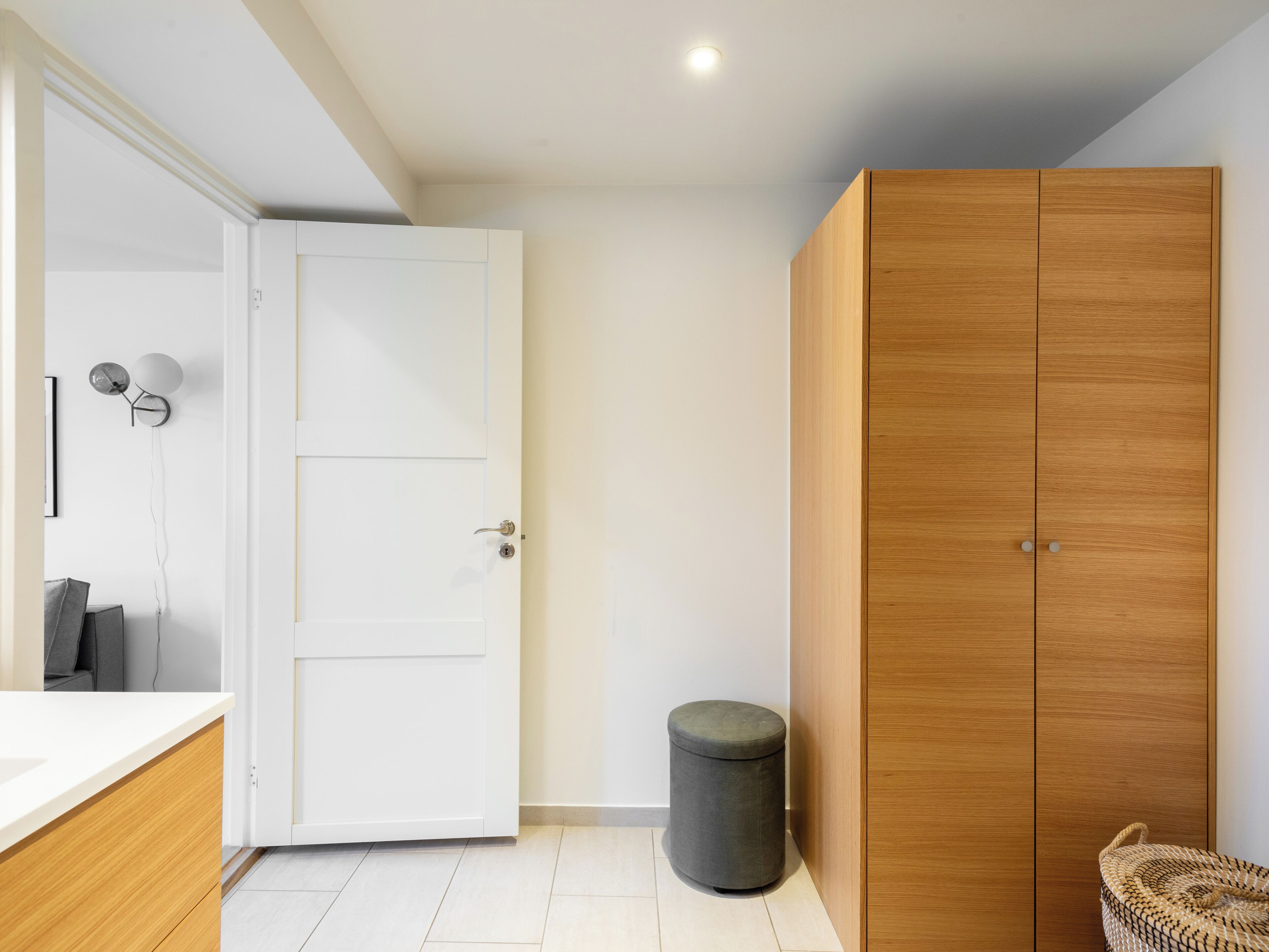 Un bagno con una porta bianca, un armadio in legno e uno sgabello grigio.