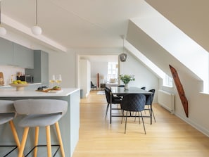 A modern kitchen with a dining area, wooden flooring, and a view of the outdoors. - Leaves 6 - 2 Bdr Apt With Shared Roof Terrace (Copenhagen)