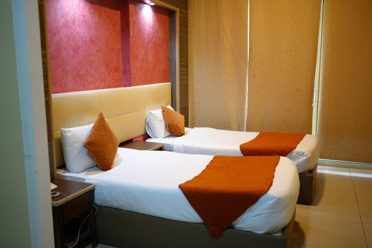Ein Hotelzimmer mit zwei Betten, jeweils mit weißen Leinentüchern und orangefarbenen Zierkissen.