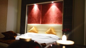 A hotel room with a large bed, two pillows, a bedside table with a vase of flowers, and a wall-mounted headboard with integrated lighting. - Elyseeresidence Hotel  (Beirut)