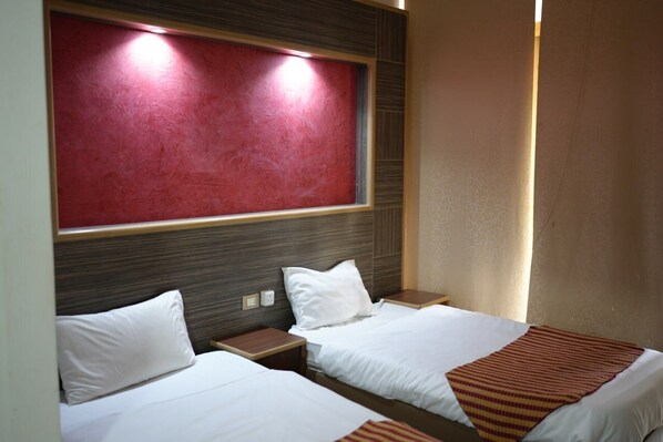 Habitación de hotel con dos camas, una pared de acento roja y una ventana con cortinas.