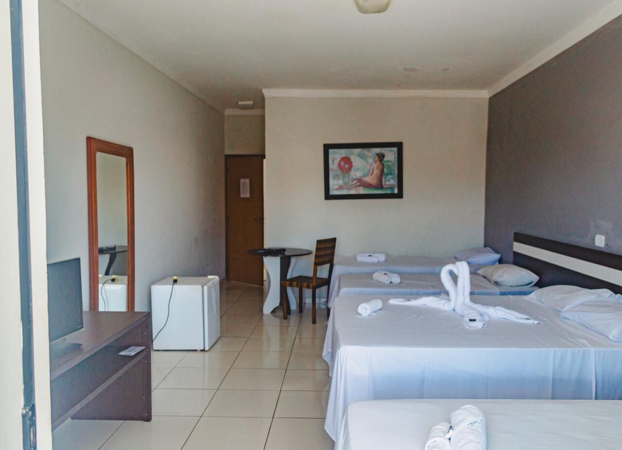 A hotel room with two beds, a desk, a chair, a small table, a television, and a painting on the wall.