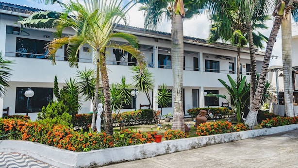 Un patio con palmeras, parterres de flores y un edificio con múltiples ventanas y balcones.