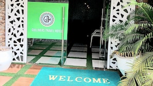 Der Eingang des Hotels Gullivers Travel, mit einer Fußmatte mit der Aufschrift 'WELCOME' und einem grünen Banner mit dem Hotel-Logo.