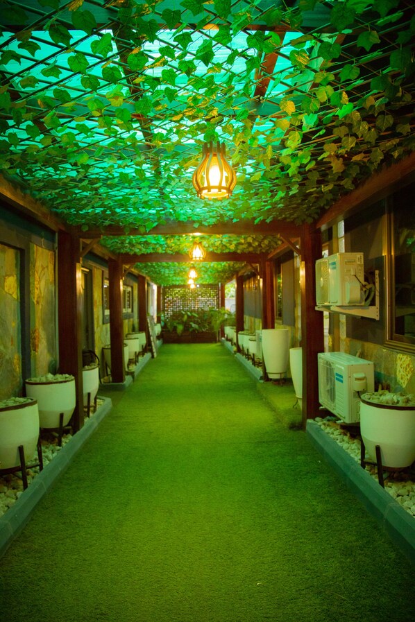A corridor with a green artificial grass floor, a hanging light fixture, and air conditioning units on the walls.