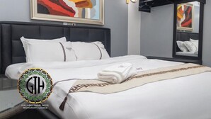 Ein Hotelzimmer mit einem Bett, einem Kopfteil, einer Wandleuchte, einem Gemälde und einem Logo.