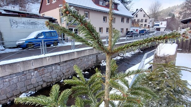 Ein Wohngebiet mit einer Stebrücke über einem Kanal, Häuser mit schneebedeckten Dächern und einem blauen Auto, das am Straßenrand geparkt ist.