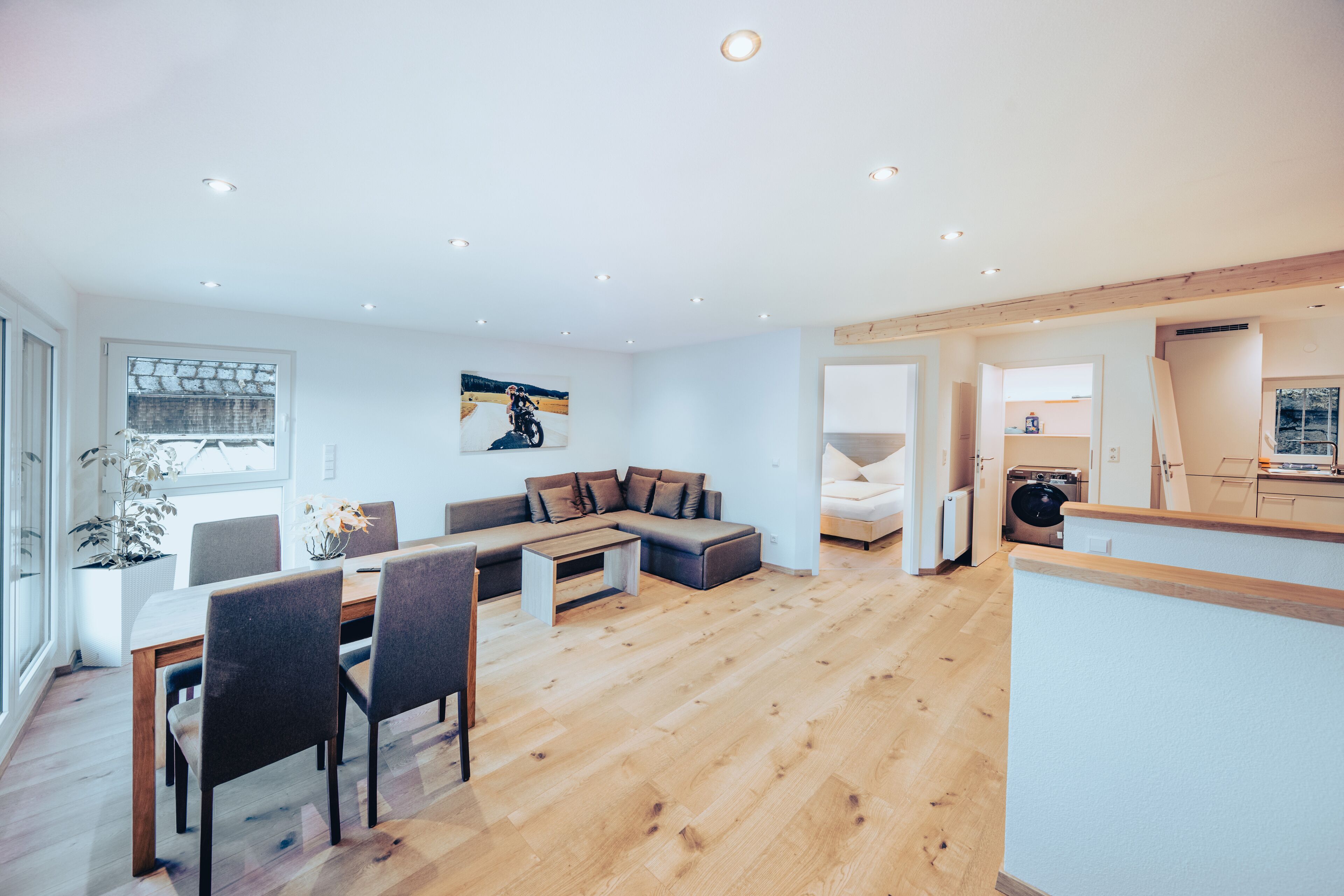 Una sala de estar moderna con piso de madera, un área de comedor con mesa y sillas, un sofá y un cuadro en la pared.