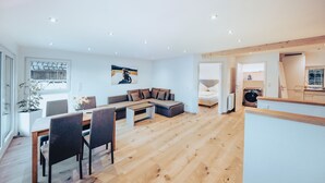 Ein modernes Wohnzimmer mit Holzboden, einem Essbereich mit Tisch und Stühlen, einem Sofa und einem Gemälde an der Wand.