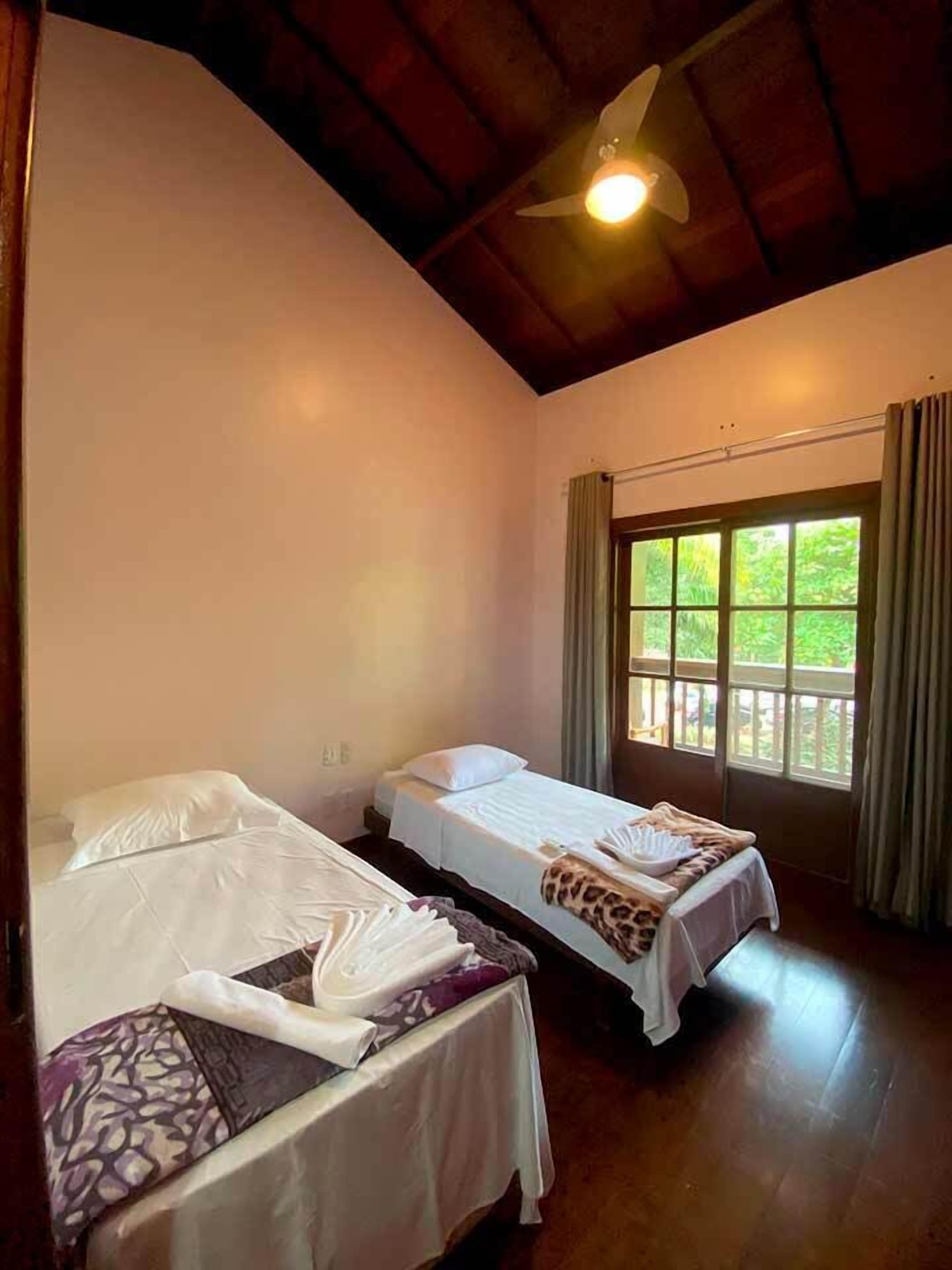 A room with two single beds, a ceiling fan, and a window with curtains.