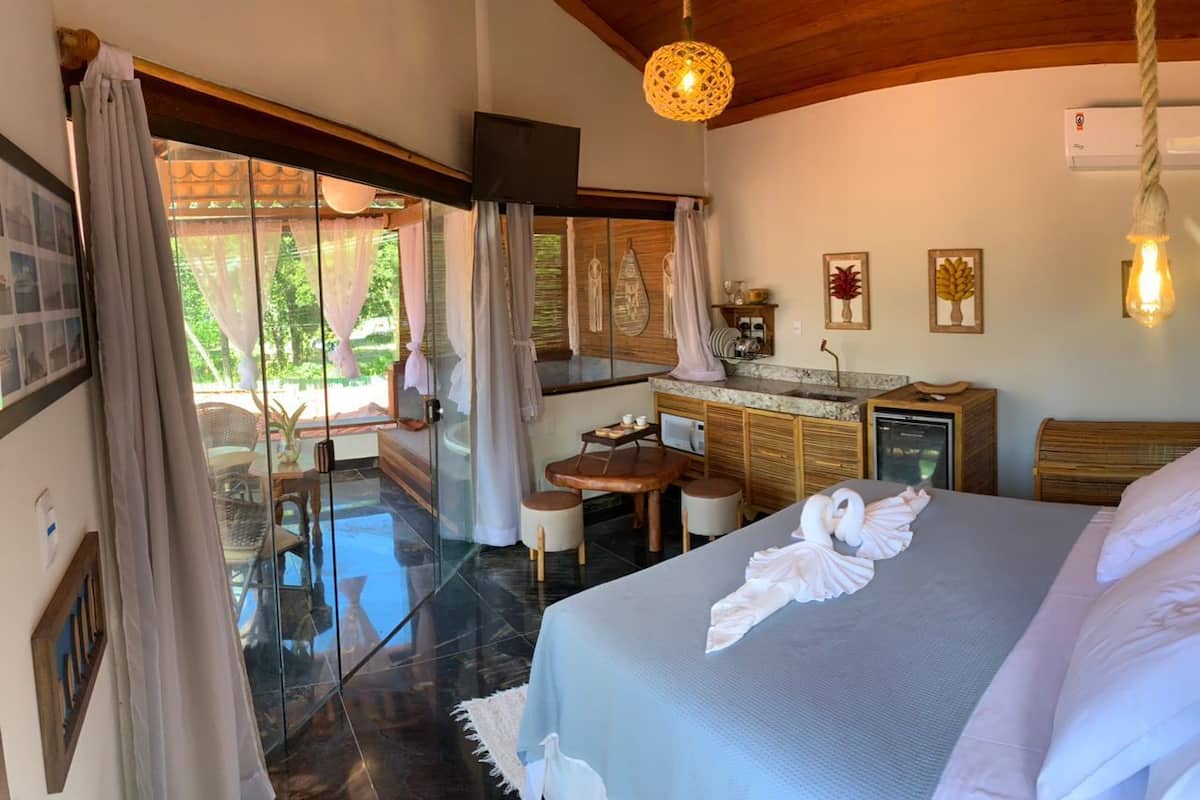 Ein Hotelzimmer mit Bett, Schreibtisch, Stuhl, kleinem Tisch, Fernseher und Blick ins Freie.